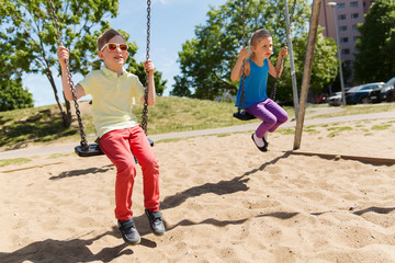 two happy kids swinging on swing at playground