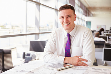 Young male architect sitting at his desk, looking to camera