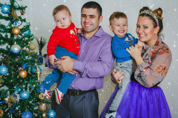 Obraz na płótnie Canvas The happy family with two small boys smiling near the New Year tree together