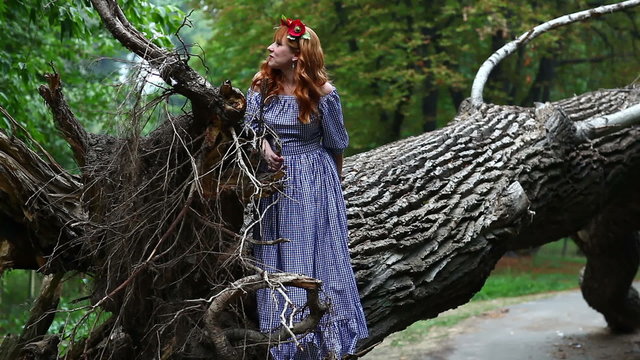 Girl with a wreath on his head. She stands near the roots of a fallen tree. 