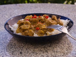 Detailed Picture of typical indian food hot lamb curry with rice and choped chili served on the deep plate or shallow bowl in the gatden on the stone granit table with silver or stainlessteel fork.