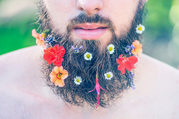 man's face with a beard with flowers in his beard close-up on green natural background, toned