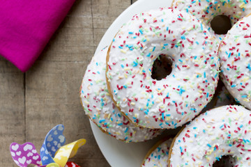 Donuts with white glaze and colorful sprinkles on rustic table
