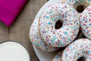 Donuts with white glaze and colorful sprinkles on rustic table