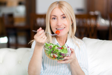 Mature woman eating a healthy salad on her sofa