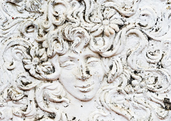 Plaster relief mural of man or woman's face with enigmatic smile and flowers in their hair
