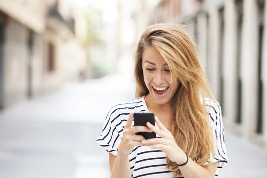 Portrait of a smiling beautiful woman typing on the smart phone with city unfocused background