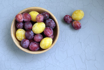Plums in a wooden plate on old  table with cracks