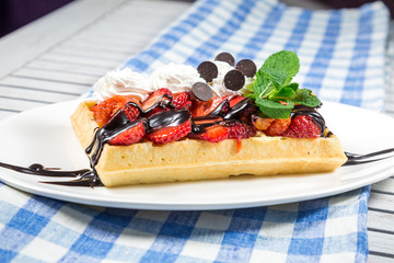 Plate of belgian waffles with ice cream, caramel sauce and fresh fruit