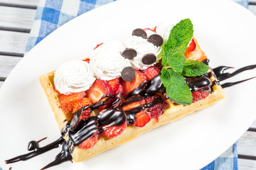 Plate of belgian waffles with ice cream, caramel sauce and fresh fruit