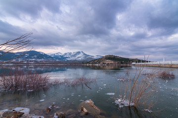 Frozen lake in winter with snowy mountains at background