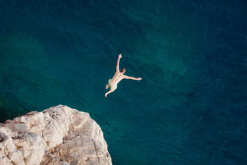 Young man jumping from cliff into sea.