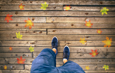 A man walking on aged wooden floor with autumn season leaves, point of view perspective. Autumn season man walk. Conceptual autumn season photo, point of view perspective used. 