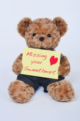 Teddy bear holding a  yellow sign saying Missing you sweetheart