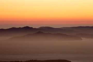 Fototapeta na wymiar Hazy sunset over Angel Island and the Marin Hills of the Golden-Gate National Recreation Area. Shot from Grizzly Peak, Berkeley Hills, California, USA.