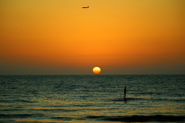 surfing at sunset with aircraft in the horizon in tel aviv, israel
