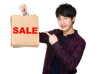 Happy young shopper with finger point to paper bag for showing a