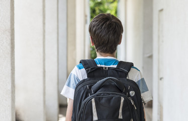 Teenage school boy with a backpack on his back walking to school. back view