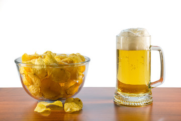Full mug of lager beer with foam and glass bowl of potato chips stand on the table on a white background
