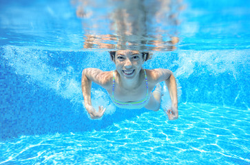 Child swims in pool underwater, happy active girl has fun in water