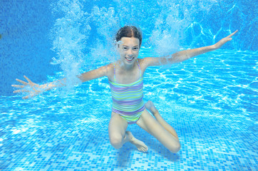 Child swims in pool underwater, happy active girl has fun in water