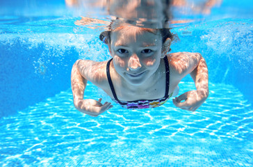 Child swims in pool underwater, happy active girl has fun in water, kid sport 