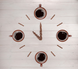 Clock made of coffee beans and cups on wooden background
