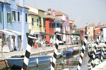 Fototapeta na wymiar In the foreground poles painted with black and white stripes in the background (out of focus) the colorful houses of Burano Island, Venice, Italy