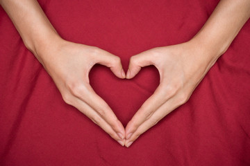 Female hands shaping a heart red background 1