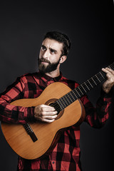 Portrait of a happy young man with beard playing guitar against
