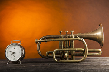 Tromba in ottone con sveglia su piano di legno e sfondo arancio