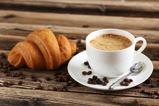 Delicious croissant with cup of coffee on brown wooden backgroun