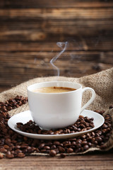Cup of coffee with coffee beans on a brown wooden background