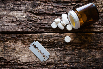 handful of pills and blade for suicide on a wooden background