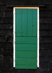 Old green wooden door with white frame and black wooden tiles