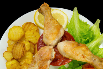 chicken legs dipped in ketchup on a white plate with lettuce and roasted potatoes view from above isolated on black background