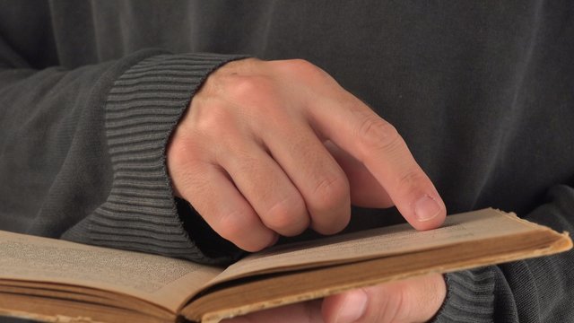 Adult man reading old vintage book with yellow pages, turning pages and looking at text, close up image with selective focus, 4k uhd footage