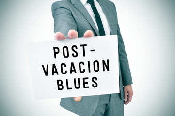 man in suit shows a signboard with the text post-vacation blues,