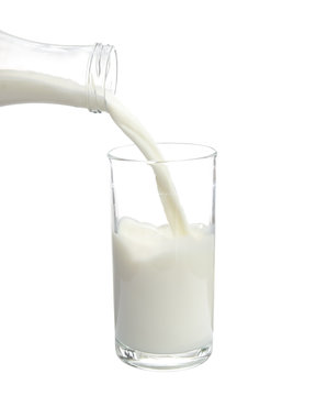 Pouring milk from bottle into glass on white background.