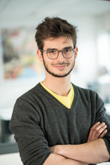  young man on his workplace, looking at camera, arms crossed