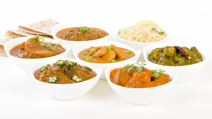 Vegetarian Curries - Selection of South Asian vegetarian curries in white bowls. Paneer Makhani, Palak Paneer, Aloo Matar, Baigan Bharta, Chilli Potatoes and Bhindi Masala, Pilau Rice and Chapattis.
