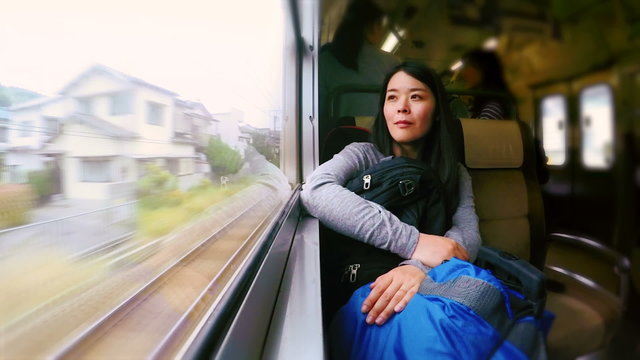 Japanese woman traveling by train looking out the window with travel bags and backpack.
