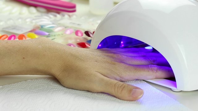 Manicure in process - putting hand and curing gel varnish in nail LED lamp, procedure of polymerization