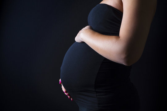 Pregnant woman stands with her hands at the belly