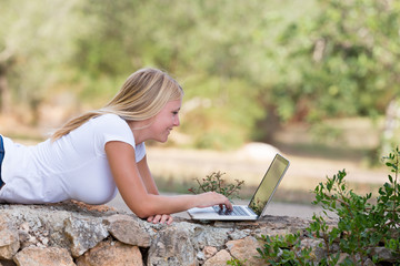 Blond teenager using laptop outdoor, selective focus