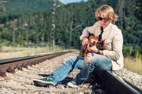 Young man with guitar on the railway