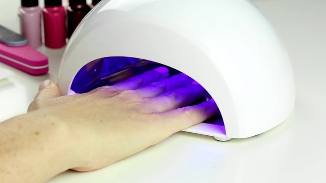 Manicure in process - putting hand and curing gel varnish in nail LED lamp, procedure of polymerization