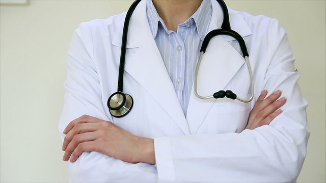 Tilt up shot of female doctor folding hands. Midsection of confident professional is wearing lab coat. She is standing in medical clinic.