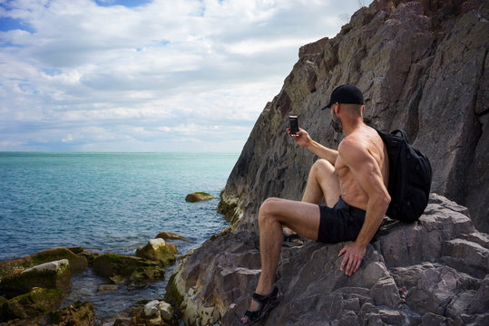A man sits on the bank of the lake and makes photos of the smartphone