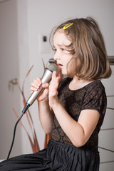 Little cute girl singing karaoke on microphone at home